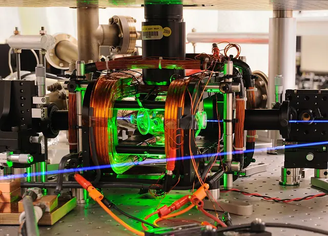 A glass chamber and microwave-control equipment, with a laser path colored blue in the source photograph.