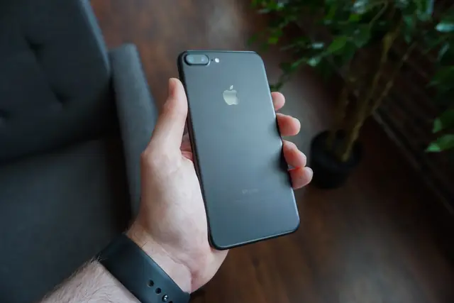 A hand holding a black smartphone with its rear camera and casing facing outward.