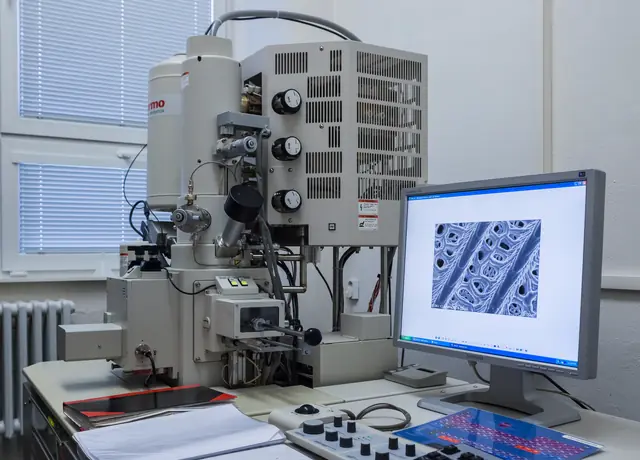 A scanning electron microscope and control monitors in a bright laboratory.