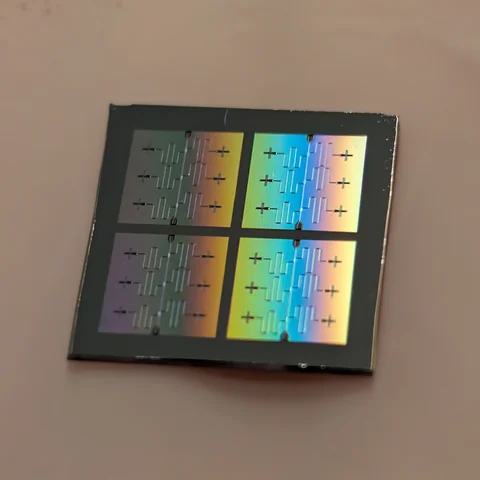 A dark square chip with four repeated patterned areas and iridescent gold and blue reflections.