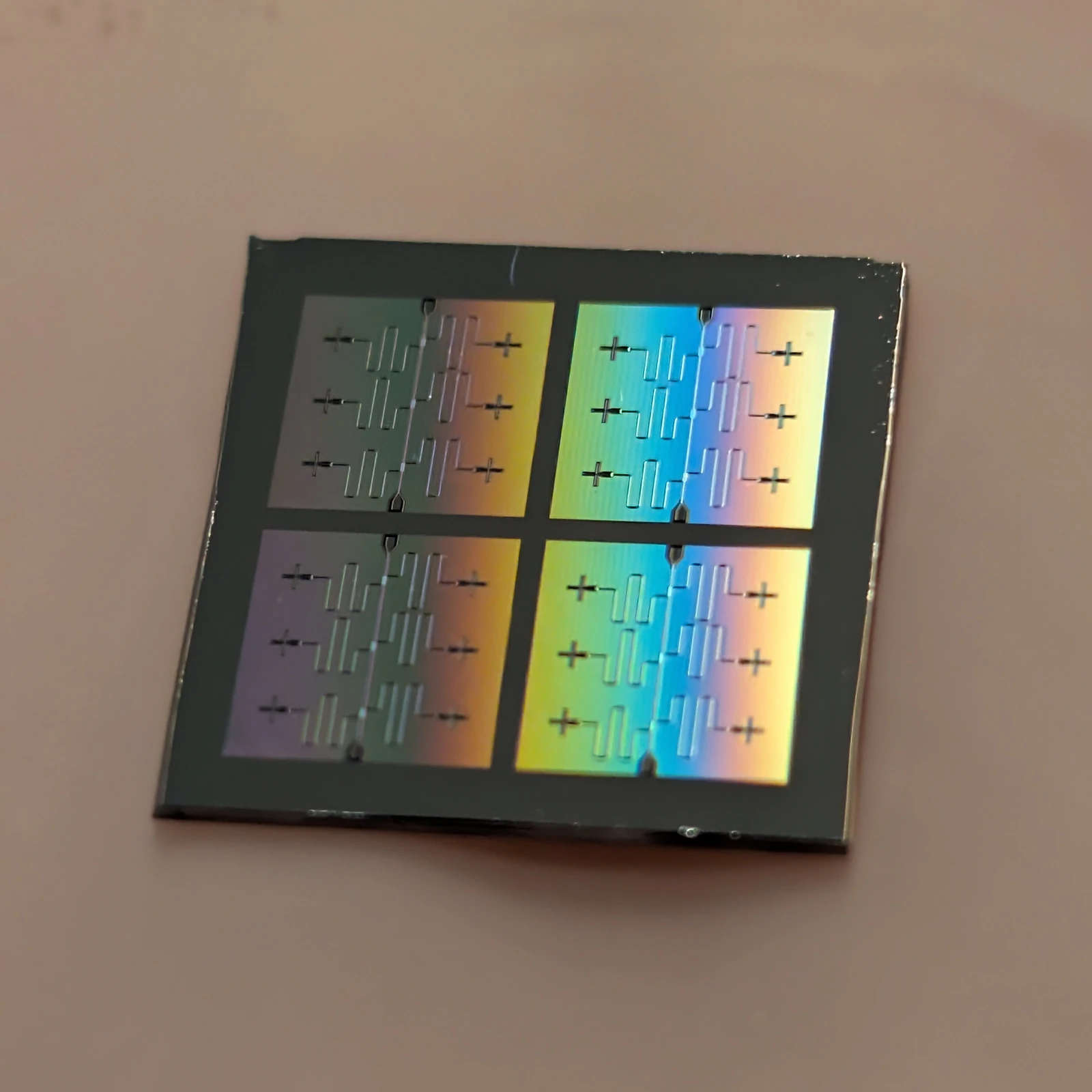 A dark square chip with four repeated patterned areas and iridescent gold and blue reflections.
