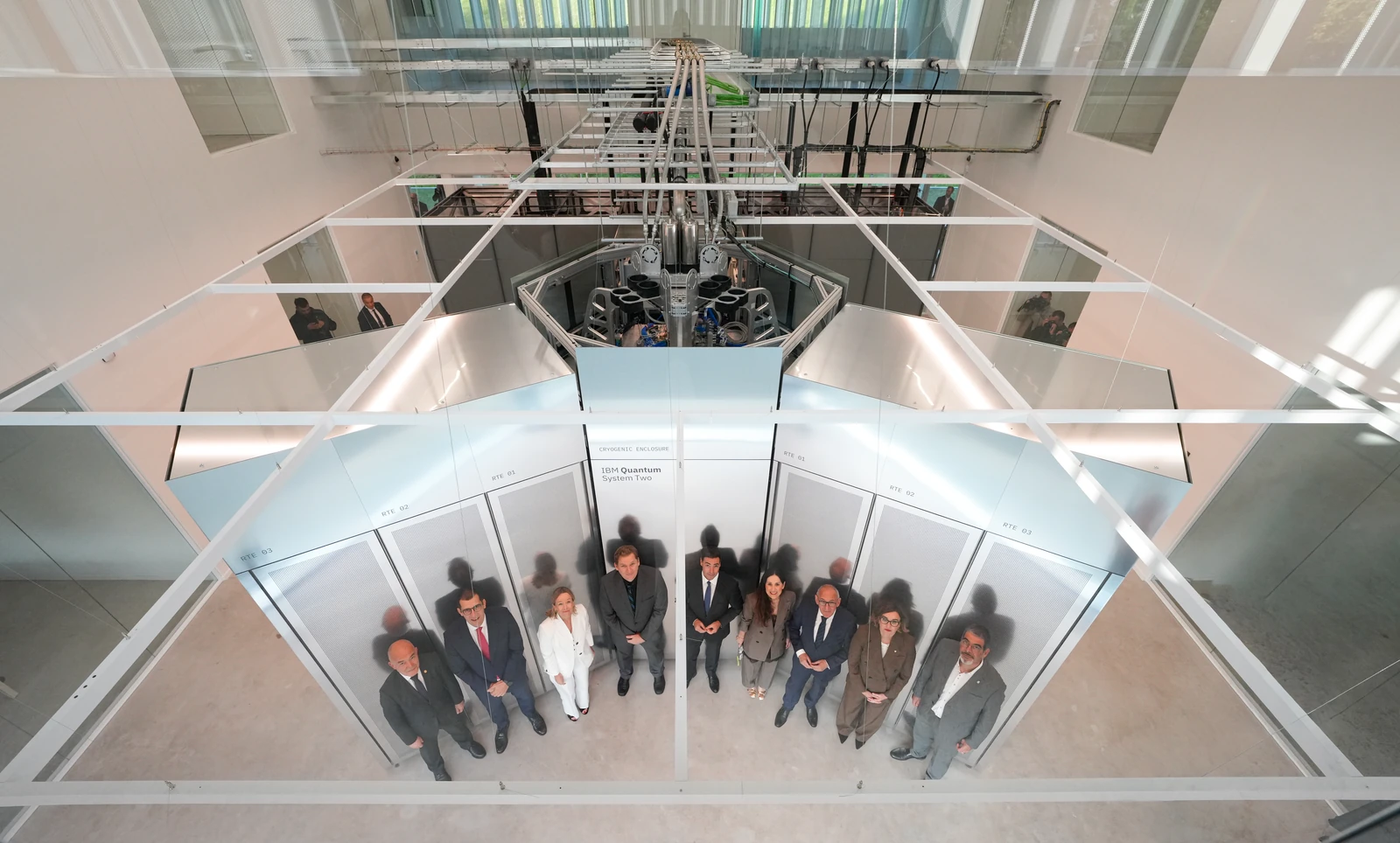 An overhead view shows mirrored and glass-walled enclosures, a suspended assembly and people gathered below.