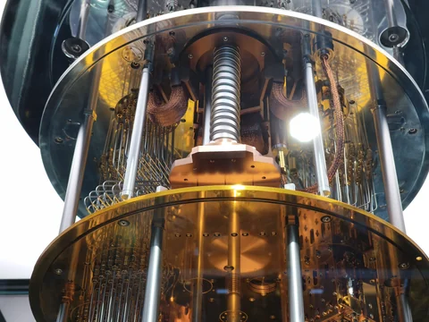 A corrugated vertical tube descends between reflective circular metal plates inside the glass display.