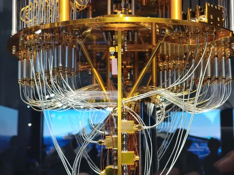Bundles of thin wires loop beneath a circular gold-colored plate and converge around vertical supports.
