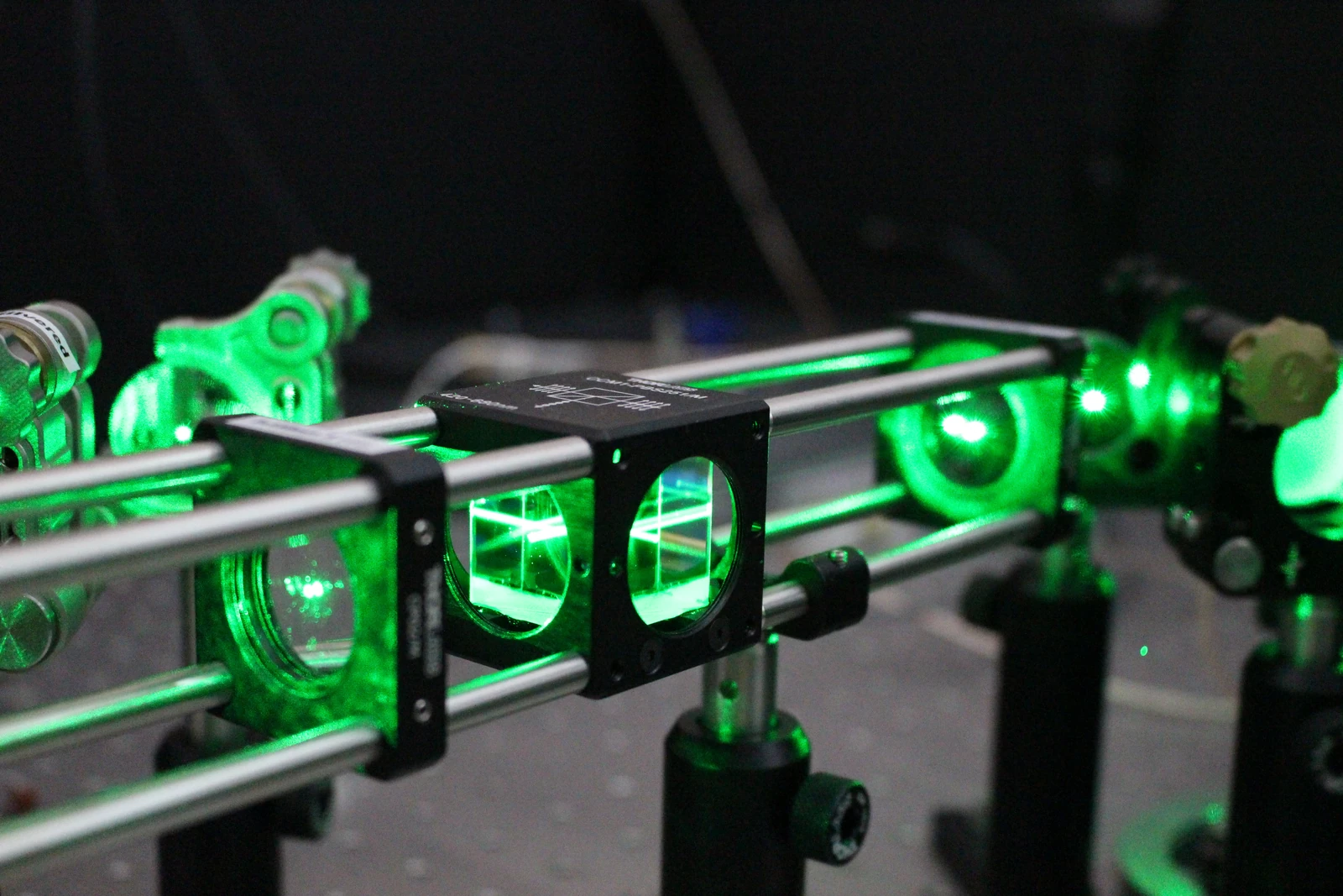 Bright green light passes through a row of small optical elements mounted on black posts against a dark background.