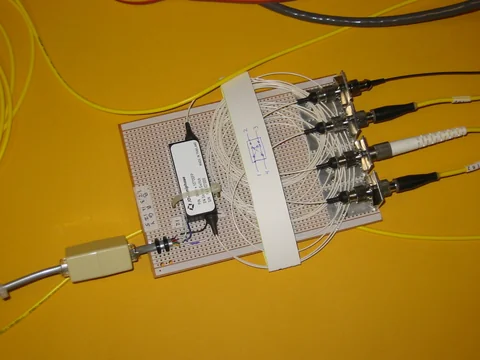 A compact circuit assembly rests on a yellow surface with multiple cables attached along one edge.
