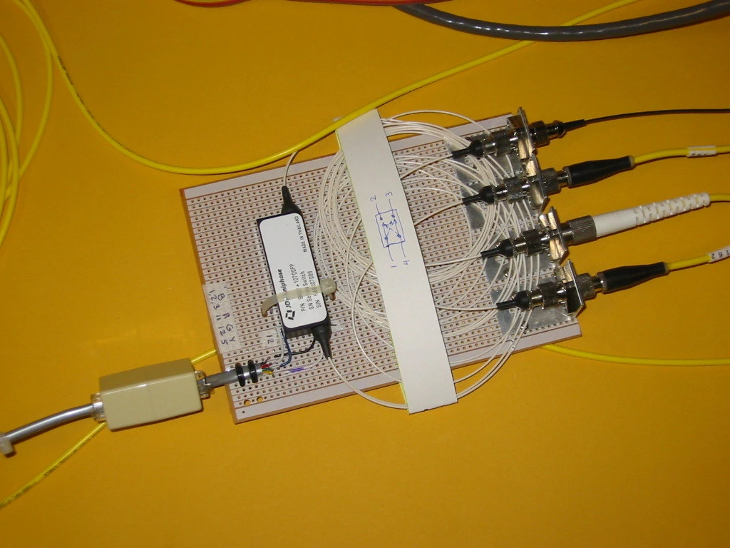 A compact circuit assembly rests on a yellow surface with multiple cables attached along one edge.