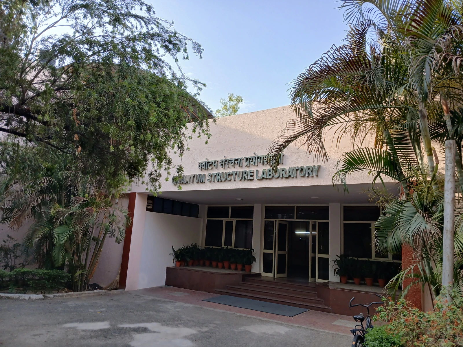 Trees and plants frame the entrance of a pale low building with laboratory lettering above the doors.