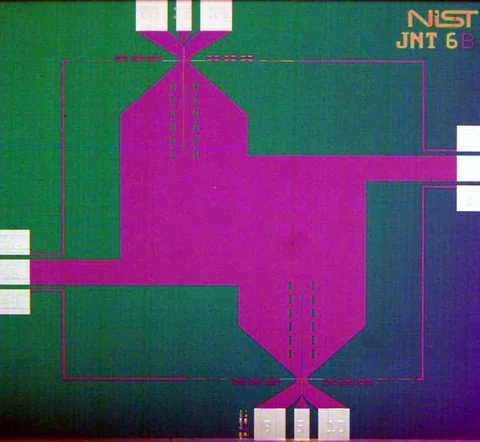 A patterned green and purple chip fills the frame, with fine lines and NIST lettering near one corner.