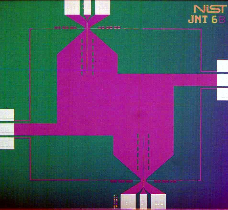 A patterned green and purple chip fills the frame, with fine lines and NIST lettering near one corner.