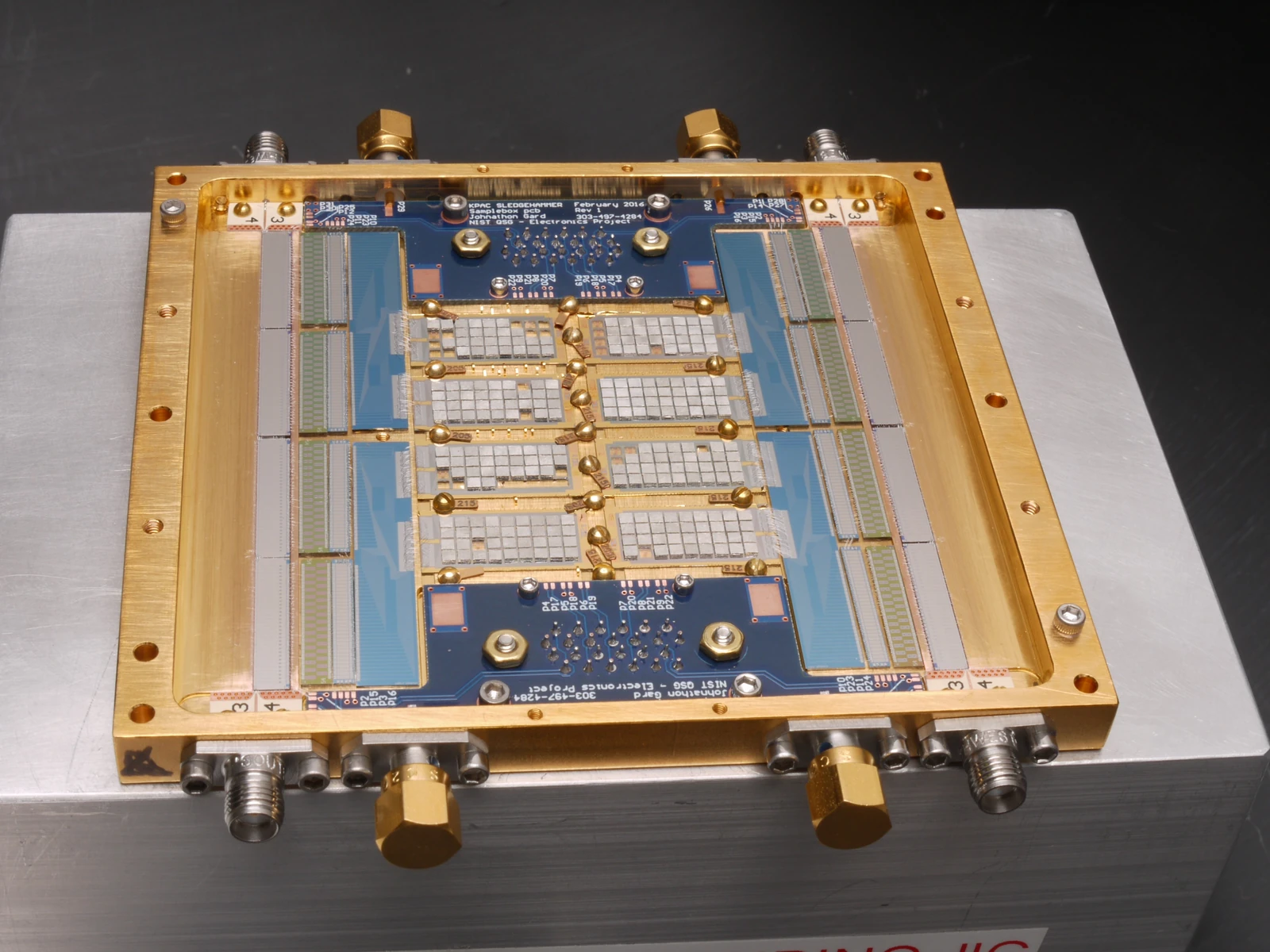 A gold rectangular frame surrounds a blue circuit board and pale rectangular sensor sections, with connectors around the gray mounting plate.