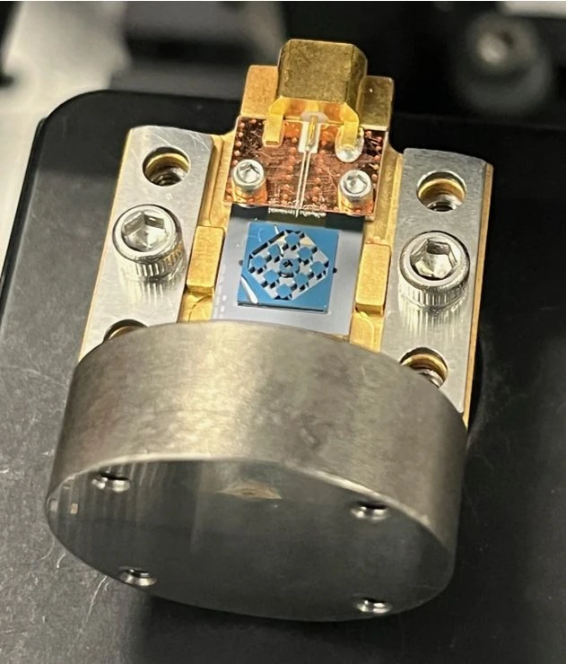 A blue square patterned component sits among gold and silver metal fittings, screws and a rounded metal mount.