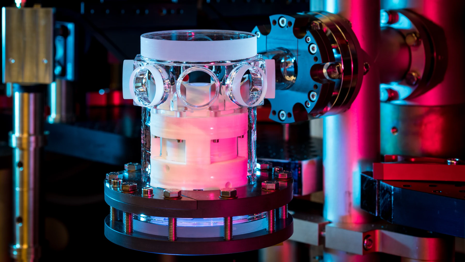 A transparent quartz-glass vacuum chamber with a microscope objective inside, lit by blue and red laboratory lights.