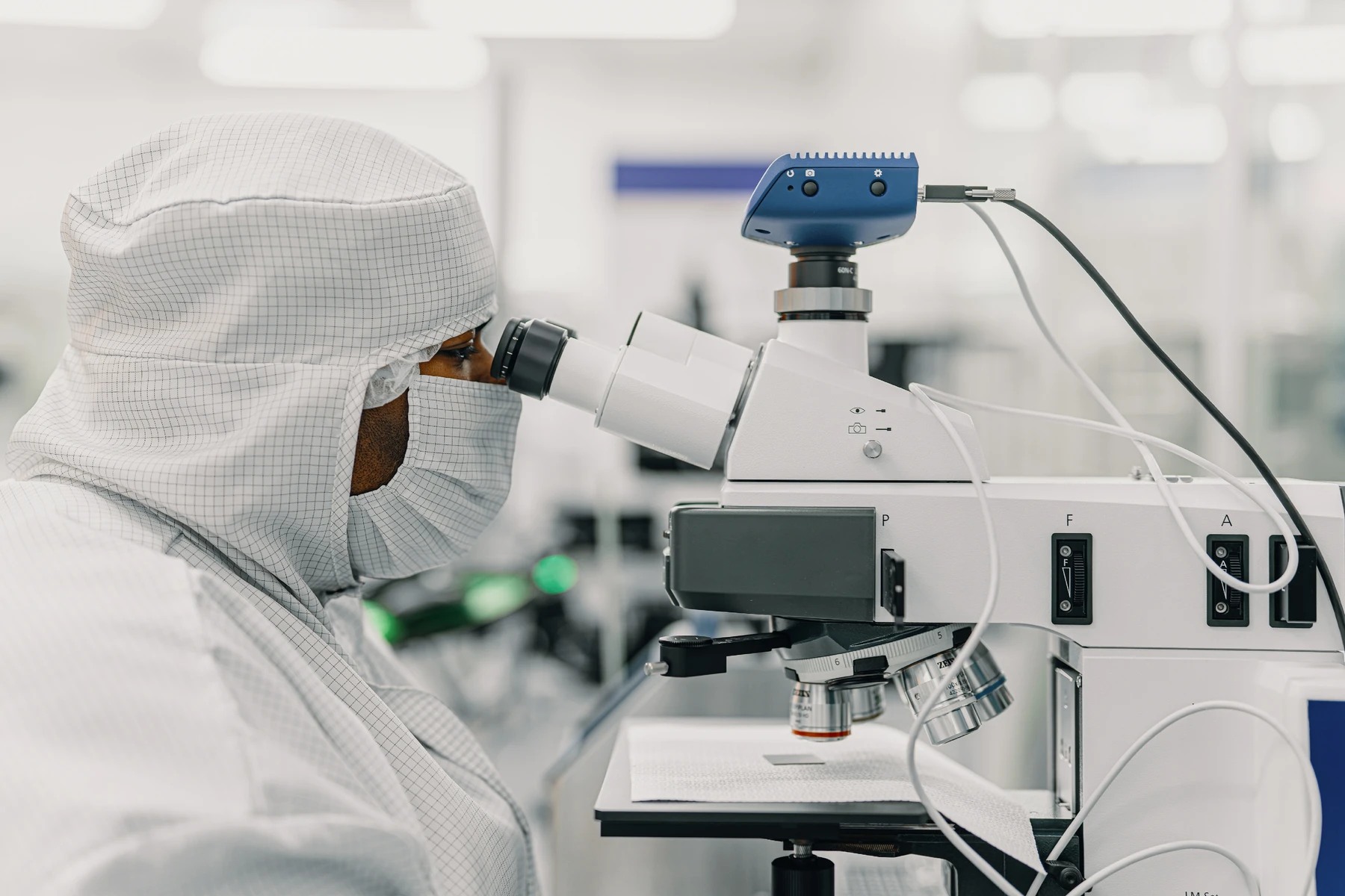 Researcher wearing cleanroom clothing looks through a microscope in an IQM facility.