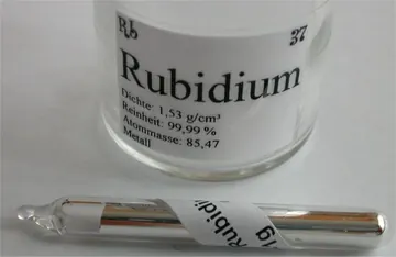 Silvery rubidium metal sealed inside a clear glass ampoule.
