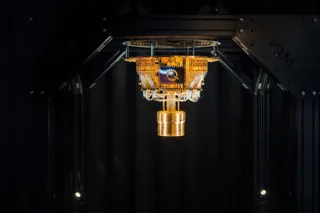 A gold-colored IQM cryogenic assembly and fine wiring hang inside a dark enclosure.