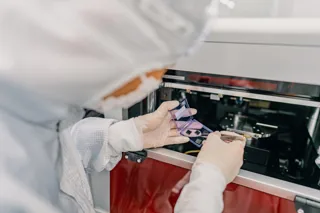 An IQM cleanroom worker handles device samples beside laboratory equipment.