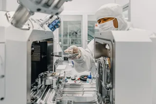 A worker in cleanroom clothing handles a wafer inside IQM laboratory equipment.