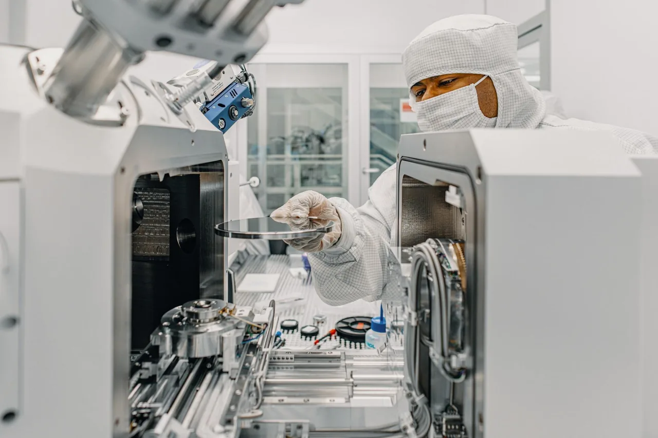 A worker in cleanroom clothing handles a wafer inside IQM laboratory equipment.
