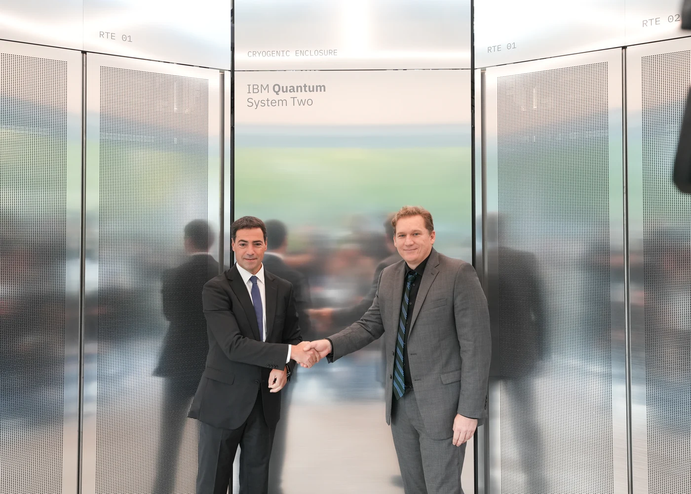 Two men shake hands in front of the reflective IBM Quantum System Two enclosure at Ikerbasque.