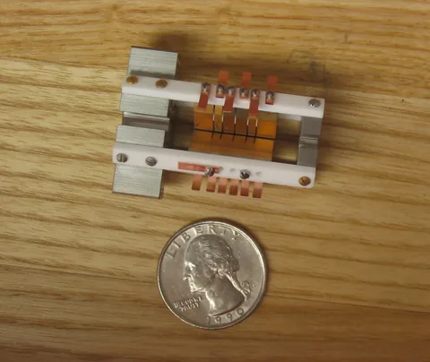 A compact ion-trap assembly on a wooden surface beside a US quarter for scale.