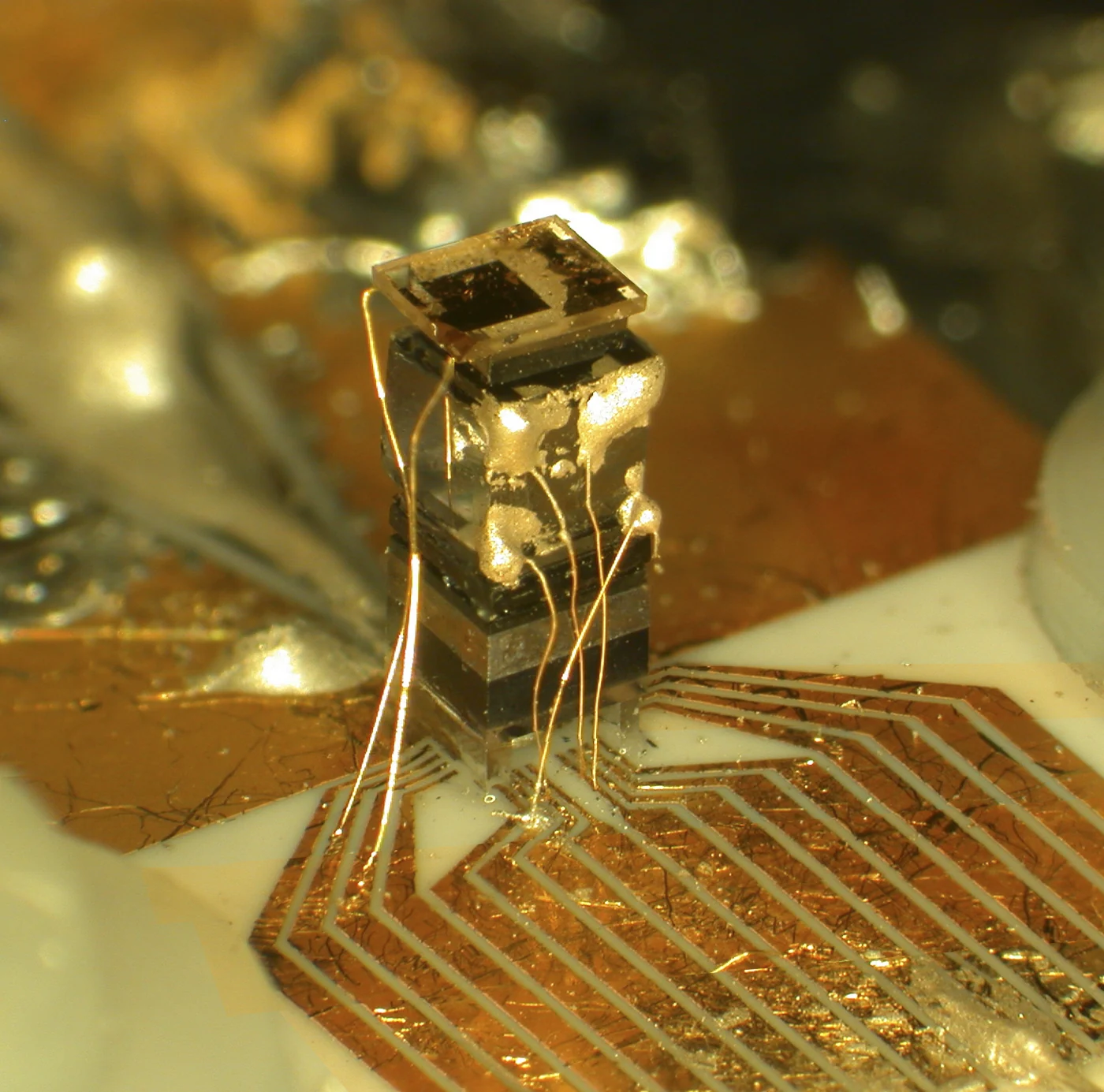 Close view of a miniature atomic-clock assembly raised above a patterned circuit surface by fine wires.