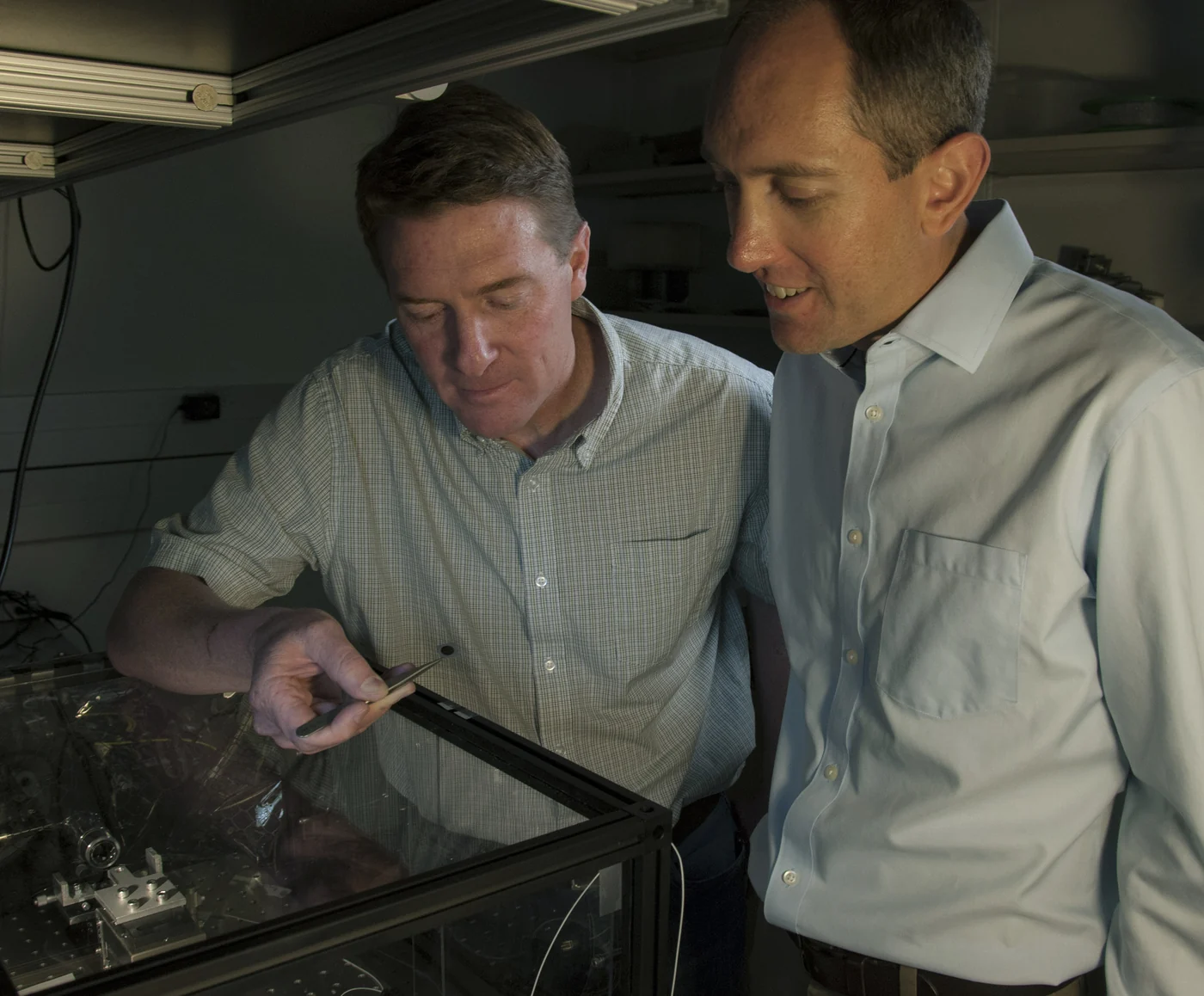 Two researchers inspect equipment together at an optical laboratory bench.