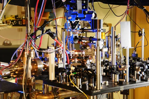 An atomic-clock laboratory apparatus with optical components, metal mounts and colored cables.