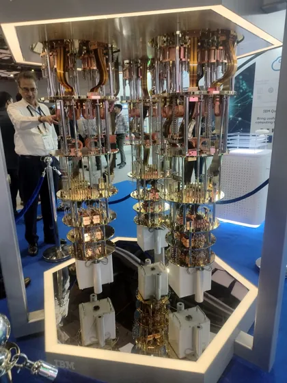 A tall exposed cryogenic-system exhibit with metal plates, wiring and surrounding visitors.