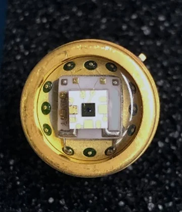A small semiconductor detector and bond wires mounted inside a round gold-colored package.