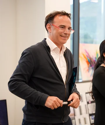 Markus Aspelmeyer holding a pen during a visit, wearing glasses, a white shirt and dark jacket.