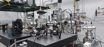 Stainless-steel vacuum chambers, viewports and optical components on a laboratory table.