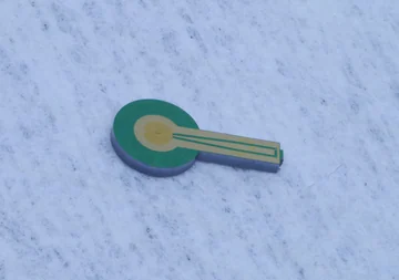 A small green-and-gold superconducting detector chip lying on a pale surface.